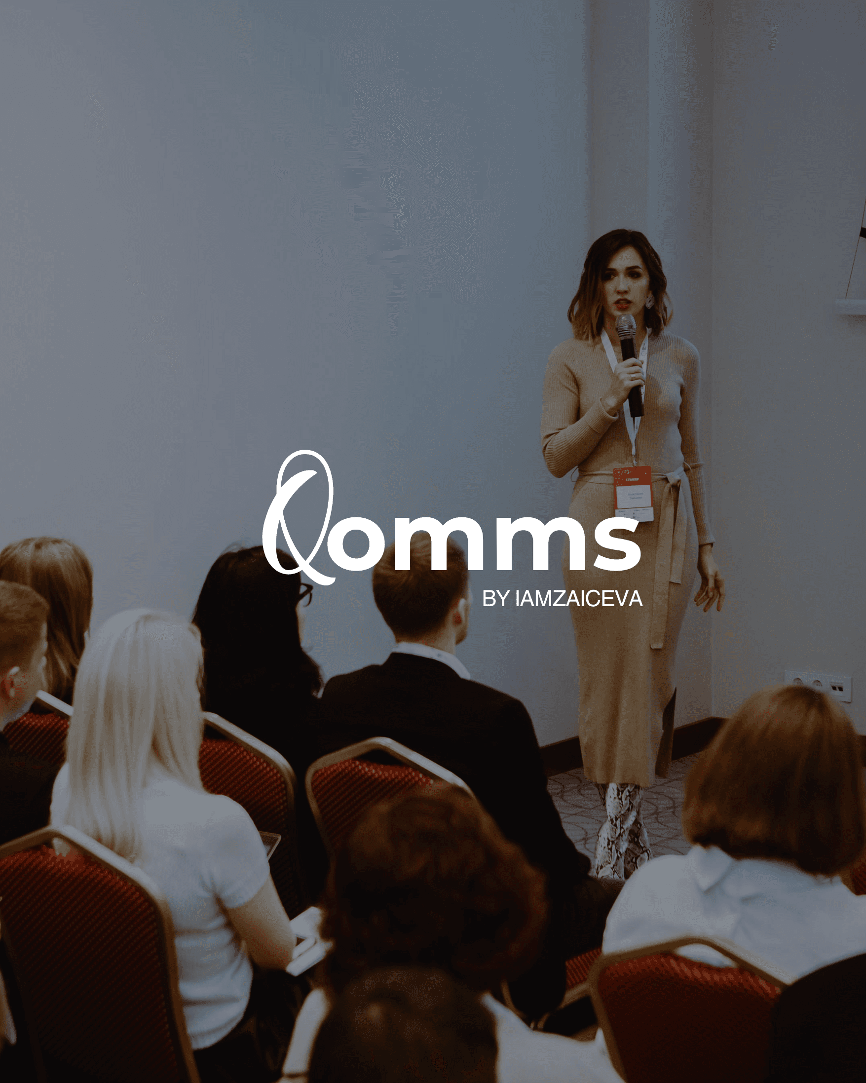 Woman speaking into a microphone at a conference with an audience and Qomms logo.